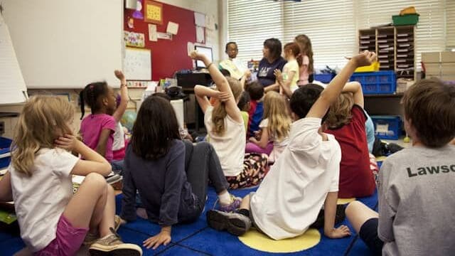 Elementary students seated on a classroom rug raising their hands during a group discussion or morning meeting